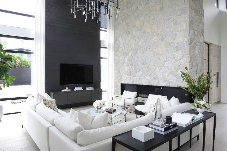 اتاق نشیمن مدرن بزرگ و لوکسی که دیوار پشت تلویزیون آن با رنگ متفاوت دیزاین شده است و مبل های سفید ال شکل و لوستر مدرن دارد